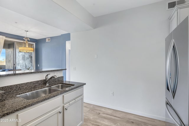 kitchen featuring white cabinetry, sink, pendant lighting, and stainless steel refrigerator