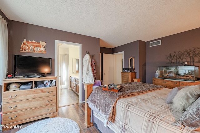 bedroom with light wood-type flooring, a textured ceiling, and connected bathroom