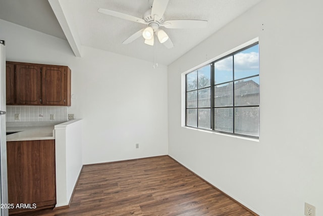 unfurnished dining area featuring dark wood-type flooring, ceiling fan, and beam ceiling