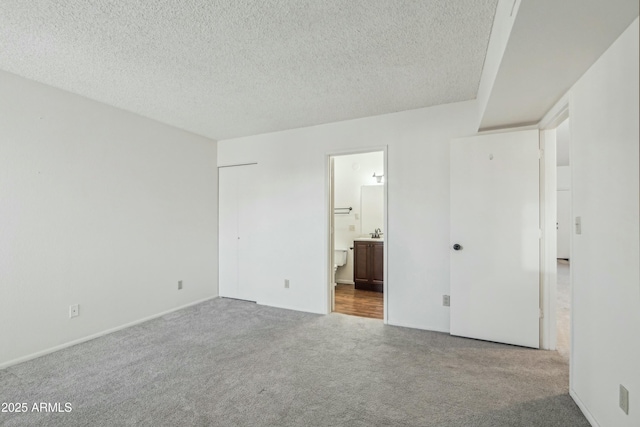 unfurnished bedroom with light carpet, a textured ceiling, and ensuite bathroom