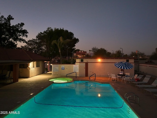 pool at dusk with a hot tub and a patio