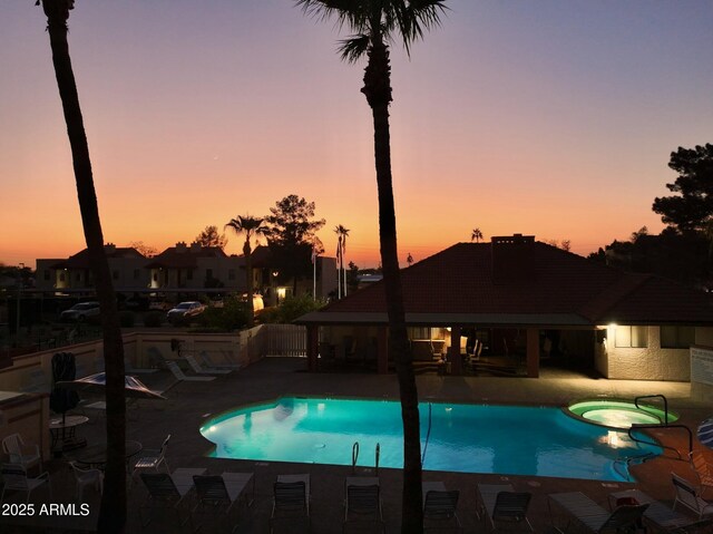 pool at dusk with a hot tub and a patio area