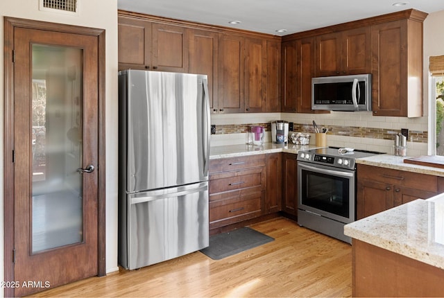 kitchen with light stone counters, appliances with stainless steel finishes, light hardwood / wood-style floors, and backsplash