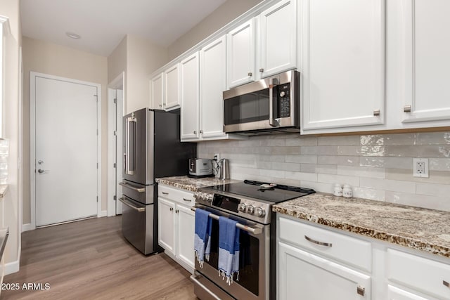 kitchen with light stone counters, backsplash, white cabinetry, light wood-style floors, and appliances with stainless steel finishes