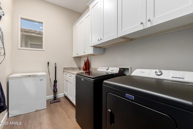 clothes washing area with cabinet space, washing machine and dryer, baseboards, and light wood finished floors