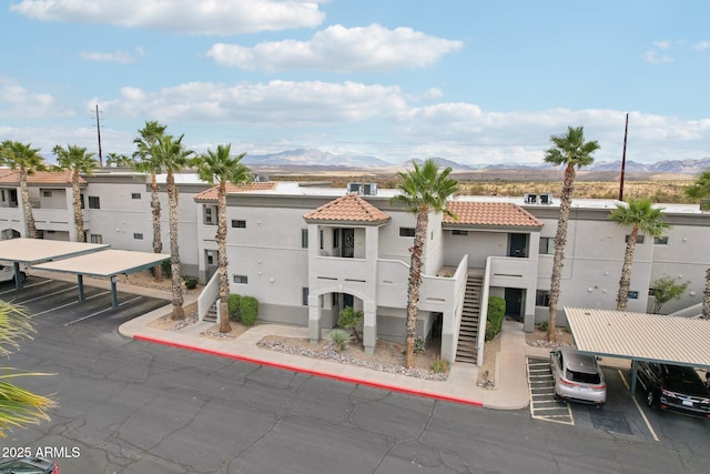 view of building exterior featuring covered parking, stairway, a residential view, and a mountain view