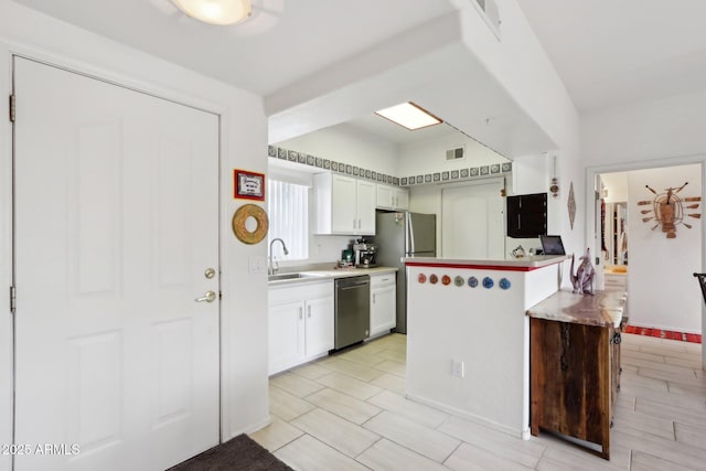 kitchen featuring visible vents, white cabinets, a peninsula, stainless steel appliances, and a sink