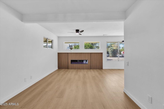 unfurnished living room featuring light wood-type flooring, baseboards, a glass covered fireplace, and a ceiling fan