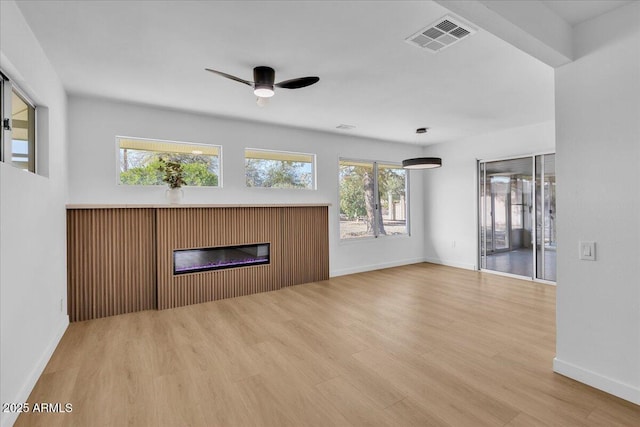 unfurnished living room with visible vents, a ceiling fan, a glass covered fireplace, wood finished floors, and baseboards