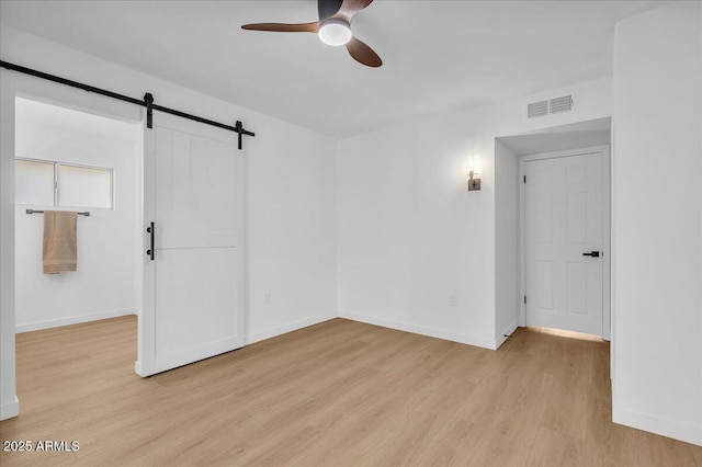 spare room featuring baseboards, visible vents, light wood finished floors, ceiling fan, and a barn door