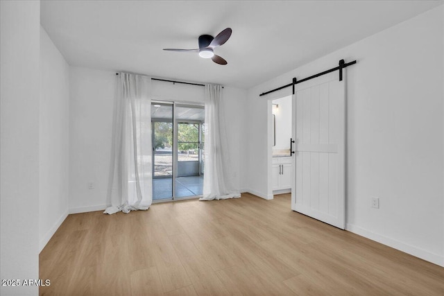 unfurnished room with baseboards, light wood-style floors, a barn door, and a ceiling fan