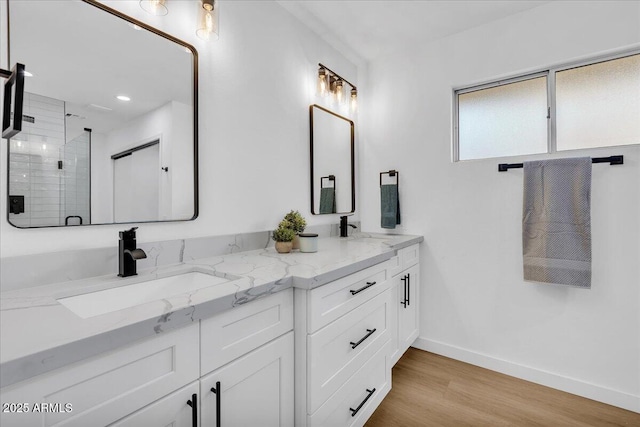 full bath with a sink, wood finished floors, a shower stall, double vanity, and baseboards