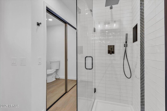 bathroom featuring baseboards, wood finished floors, toilet, and a stall shower