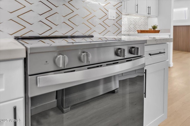 interior details featuring stainless steel range oven, light wood finished floors, tasteful backsplash, and white cabinetry