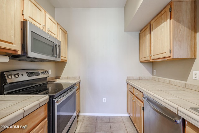 kitchen with tile countertops, light brown cabinets, light tile patterned floors, and stainless steel appliances