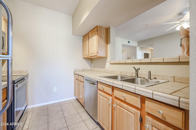 kitchen featuring tile countertops, sink, ceiling fan, light tile patterned floors, and stainless steel appliances