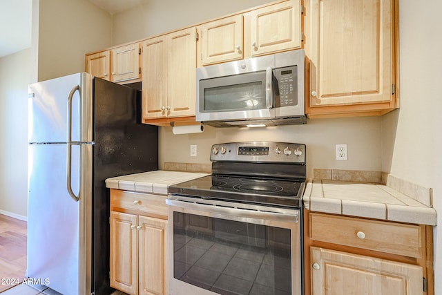 kitchen with tile countertops, light brown cabinetry, light hardwood / wood-style flooring, and appliances with stainless steel finishes