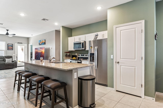 kitchen featuring a kitchen bar, sink, stainless steel appliances, light stone countertops, and white cabinets