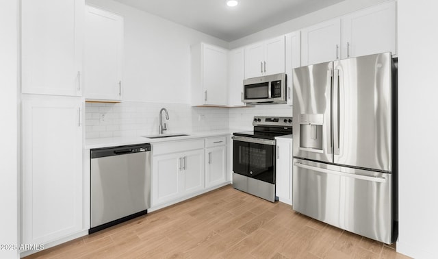 kitchen featuring white cabinets, a sink, stainless steel appliances, light countertops, and backsplash