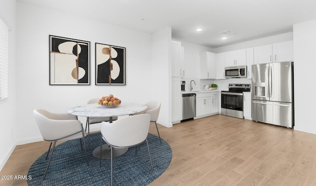 kitchen with light wood finished floors, appliances with stainless steel finishes, light countertops, white cabinetry, and a sink