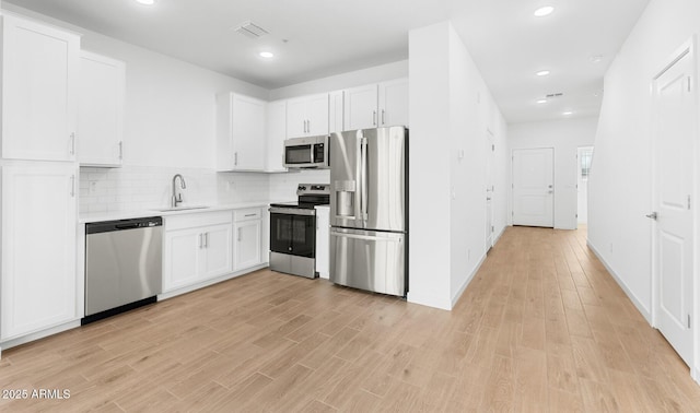 kitchen featuring light wood-type flooring, appliances with stainless steel finishes, white cabinets, and a sink