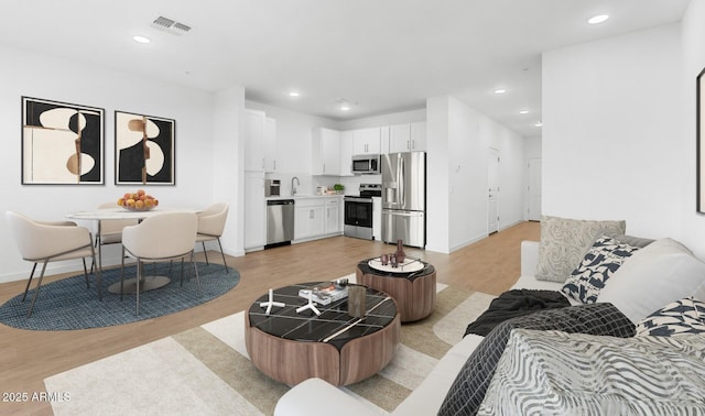 living area featuring baseboards, light wood finished floors, visible vents, and recessed lighting