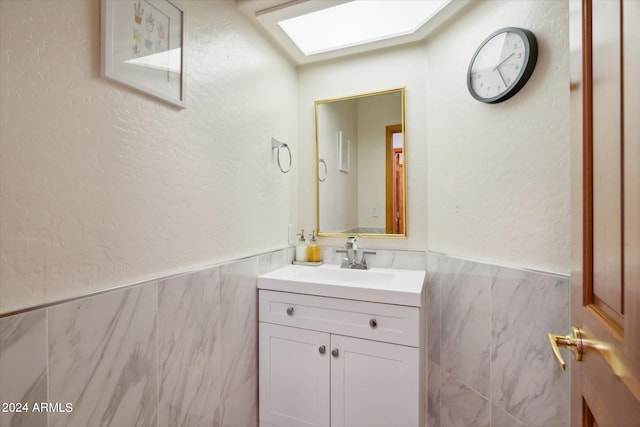 bathroom with vanity, a skylight, and tile walls