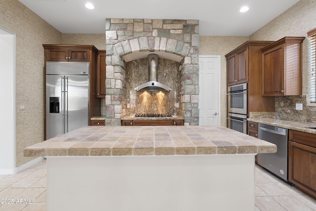 kitchen with stainless steel appliances, a kitchen island, light tile patterned floors, and wall chimney exhaust hood