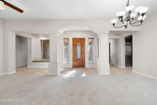 carpeted foyer entrance with ceiling fan with notable chandelier and decorative columns