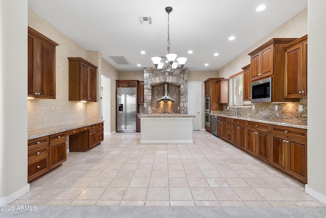 kitchen with built in appliances, a center island, light stone countertops, and decorative light fixtures