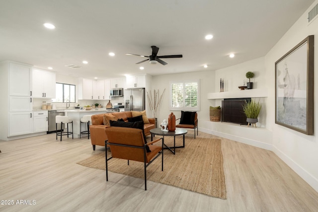 living area featuring a wealth of natural light, visible vents, light wood-type flooring, and a fireplace with raised hearth