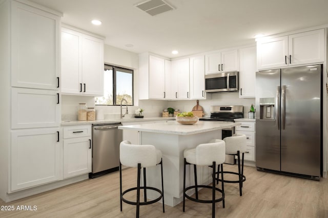 kitchen featuring visible vents, a kitchen island, white cabinetry, stainless steel appliances, and a breakfast bar area