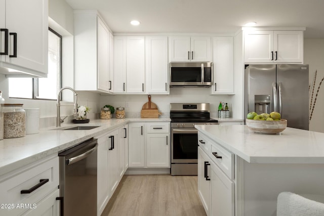 kitchen with white cabinetry, light stone countertops, appliances with stainless steel finishes, and a sink