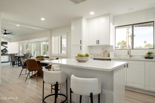 kitchen featuring light wood finished floors, a kitchen island, a sink, white cabinets, and a kitchen bar