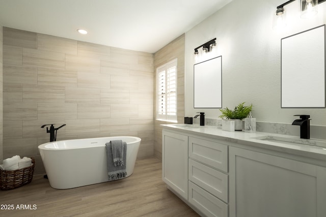 full bath featuring double vanity, a freestanding tub, wood finished floors, and a sink