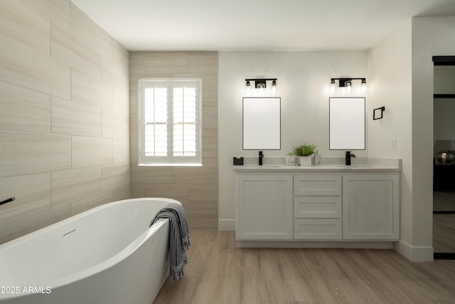 bathroom with double vanity, a soaking tub, a sink, and wood finished floors