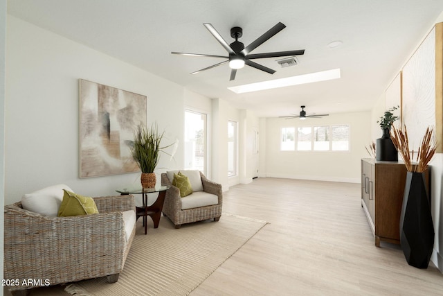 sitting room featuring visible vents, light wood-style floors, a skylight, baseboards, and ceiling fan