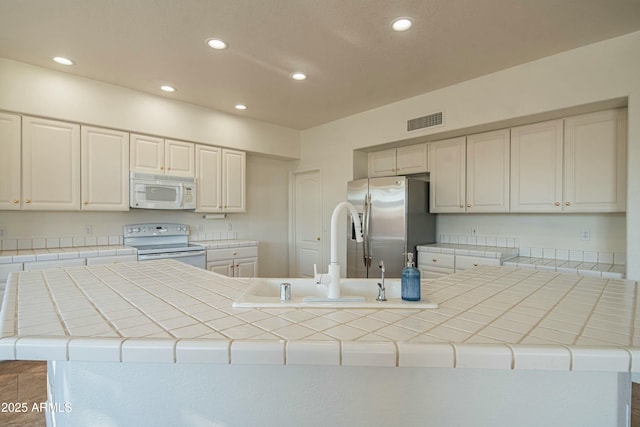 kitchen featuring sink, white appliances, a kitchen island with sink, tile counters, and white cabinets