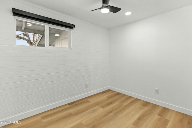 spare room featuring hardwood / wood-style flooring, brick wall, and ceiling fan