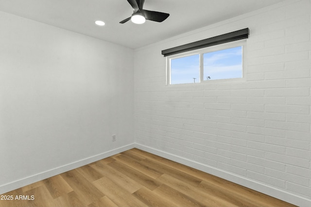 unfurnished room with hardwood / wood-style flooring, ceiling fan, and brick wall