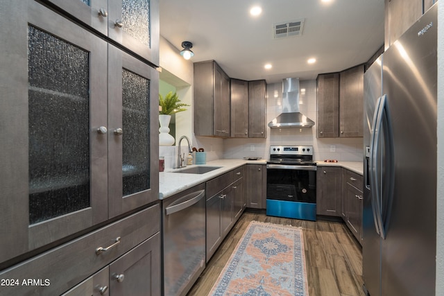 kitchen featuring appliances with stainless steel finishes, tasteful backsplash, wall chimney exhaust hood, sink, and hardwood / wood-style flooring