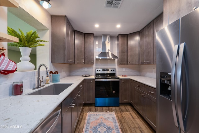 kitchen with light stone countertops, wall chimney exhaust hood, stainless steel appliances, sink, and dark hardwood / wood-style floors