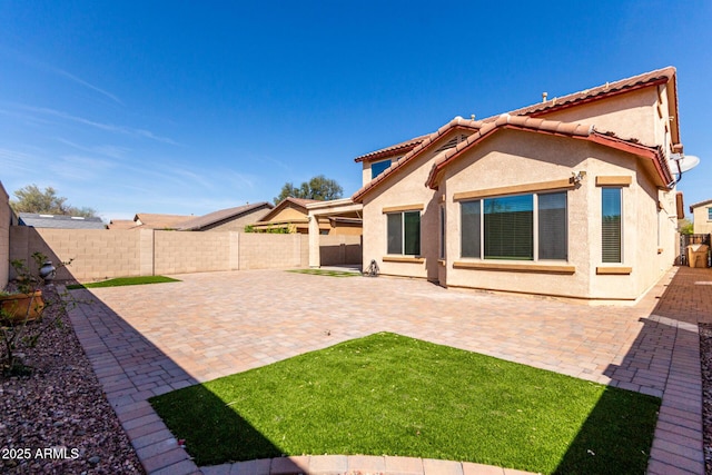rear view of house with a fenced backyard, a tiled roof, stucco siding, and a patio area
