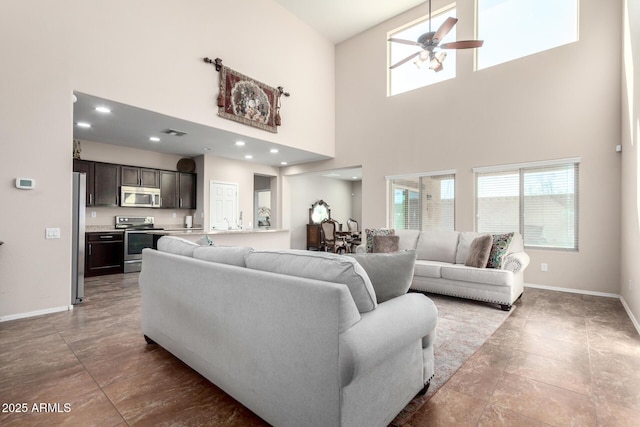 living area with baseboards, a high ceiling, visible vents, and a ceiling fan