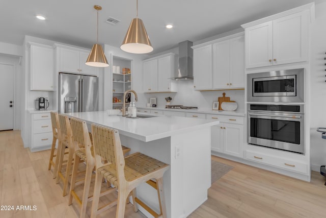 kitchen with appliances with stainless steel finishes, decorative light fixtures, white cabinets, and wall chimney exhaust hood