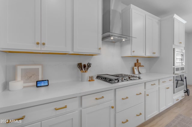 kitchen featuring white cabinetry, appliances with stainless steel finishes, wall chimney range hood, and light wood-type flooring