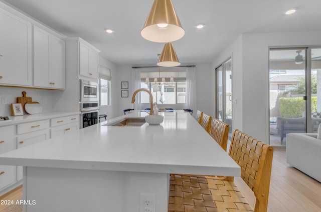 kitchen featuring a kitchen bar, sink, pendant lighting, stainless steel appliances, and a kitchen island with sink