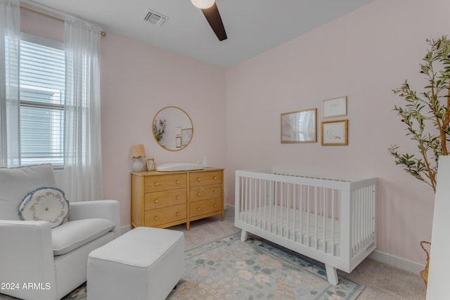 carpeted bedroom with a crib and ceiling fan