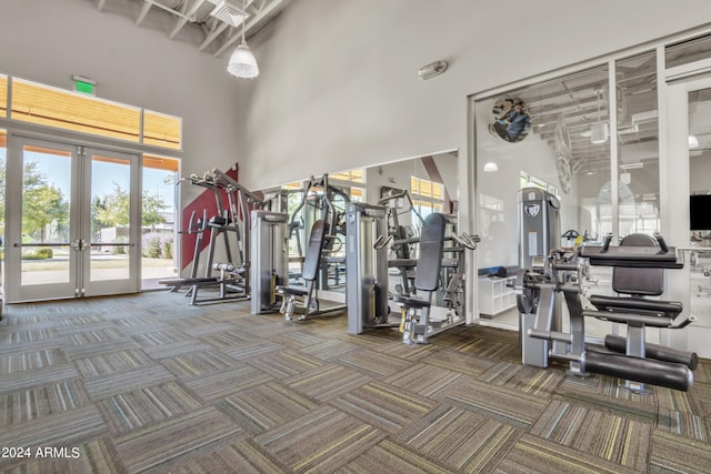 exercise room featuring a towering ceiling, dark carpet, and french doors