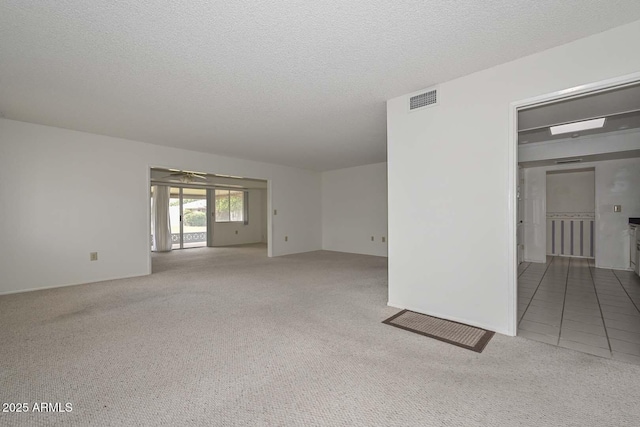 spare room with visible vents, a ceiling fan, a textured ceiling, carpet flooring, and tile patterned flooring